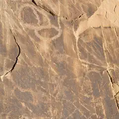 Rock art panel features abstract designs and possible human figures on dark stone surface; eroded over time with visible wear.
