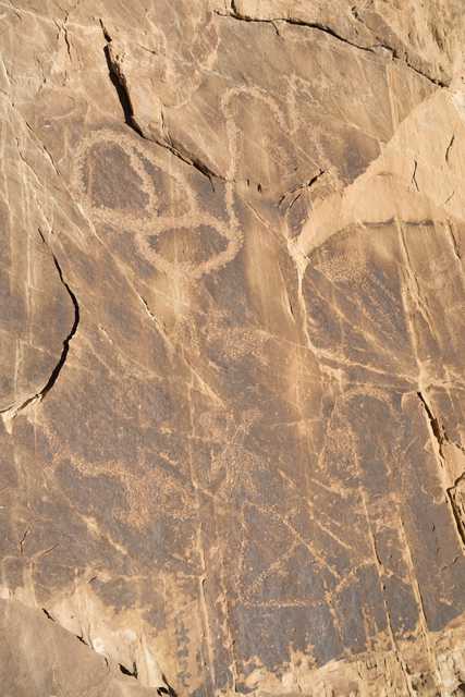 Rock art panel features abstract designs and possible human figures on dark stone surface; eroded over time with visible wear.