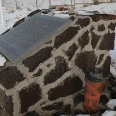 A stone monument with a plaque and a fire hydrant next to it, surrounded by snow-covered ground.
