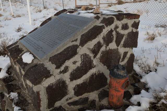 A stone monument with a plaque and a fire hydrant next to it, surrounded by snow-covered ground.