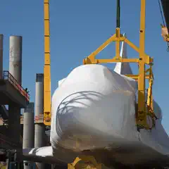 An orbiter is suspended from a yellow crane, wrapped in white plastic sheeting.