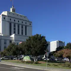A large white building stands behind a grassy area with several trees and tents.