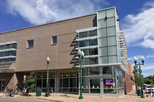 A tan-brick building with glass windows and street lamps in front of it.