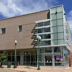 A tan-brick building with glass windows and street lamps in front of it.