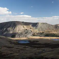 An open area with small pools of water lies before a mountainous landscape.