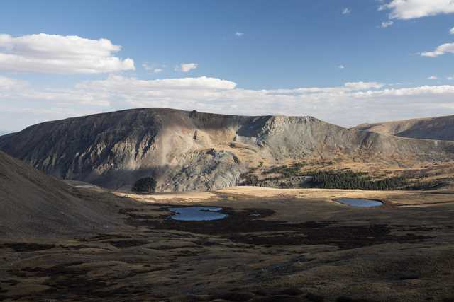 An open area with small pools of water lies before a mountainous landscape.