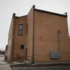 An old brick building constructed from red bricks, featuring a door and two windows on the visible side.