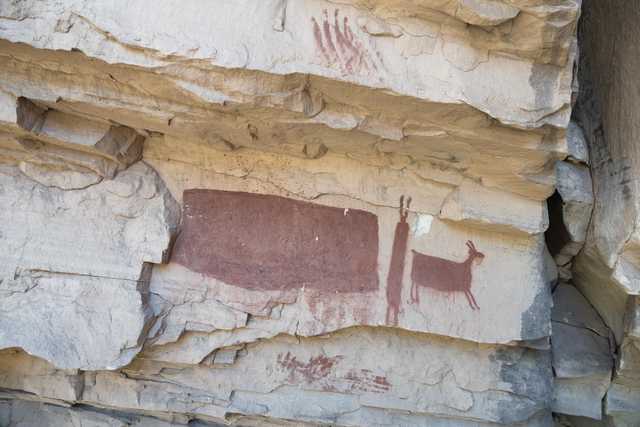 A large rock formation features red paintings of animals and handprints.