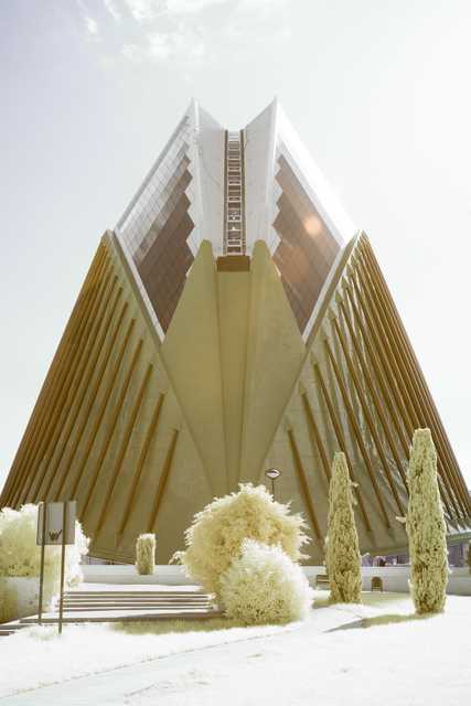 An angular building with a glass facade is visible behind a row of trees.