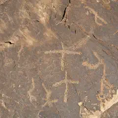A rock face features a collection of petroglyphs that appear to be ancient animal or human figures.