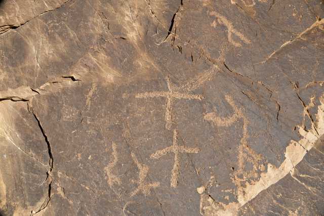 A rock face features a collection of petroglyphs that appear to be ancient animal or human figures.
