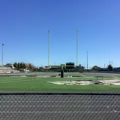 A football field with goalposts and a scoreboard, viewed from behind a chain-link fence.