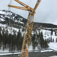 A yellow crane stands over a snowy landscape, its boom extending into the sky.