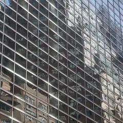 A modern glass facade reflects the distorted image of a nearby brick building.