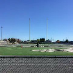 A football field with goalposts and a scoreboard, viewed from behind a chain-link fence.