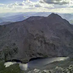A rocky mountain peak with patches of vegetation overlooking a calm lake.