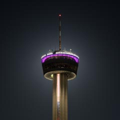 A tall tower with a circular observation deck illuminated by purple and white lights.
