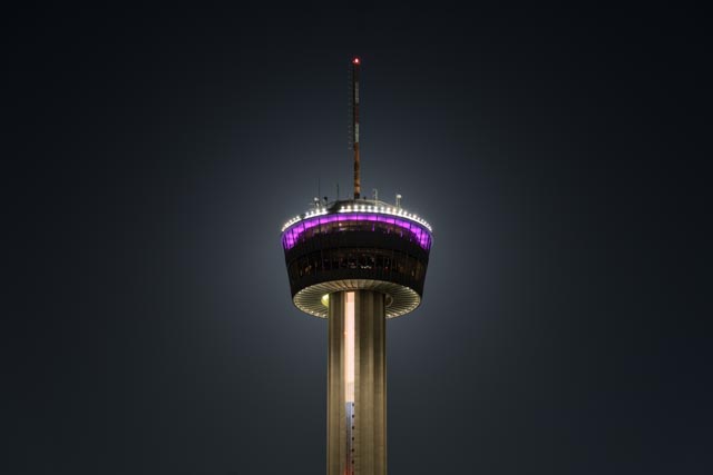 A tall tower with a circular observation deck illuminated by purple and white lights.
