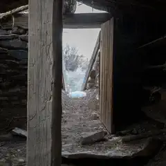 An old, dilapidated building interior with exposed wooden beams and stone walls.
