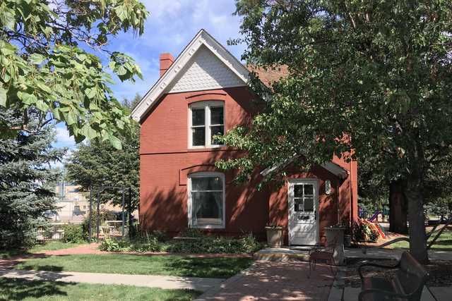 A red two-story house with a white door and window frames, surrounded by grass and trees, under a partly cloudy sky.