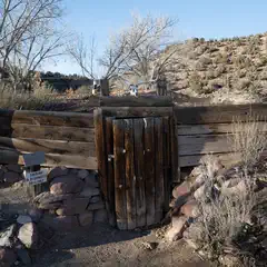 A rustic wooden gate with a stone base and a backdrop of rocky terrain under a clear sky.