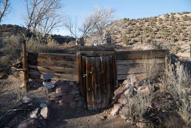 A rustic wooden gate with a stone base and a backdrop of rocky terrain under a clear sky.