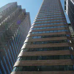 A tall building with horizontal brick bands and reflective windows is centered. A zigzag-patterned building is on the left. A building is partially visible on the right.