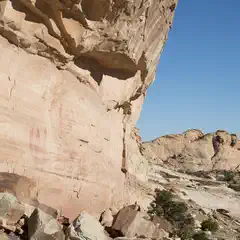 A large rock formation with red markings, set against a clear blue sky and surrounded by arid landscape.