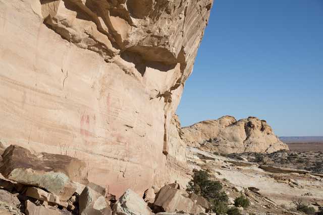 A large rock formation with red markings, set against a clear blue sky and surrounded by arid landscape.