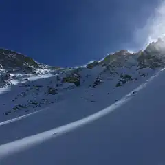 Snow-covered peaks and rocky outcrops under a clear blue sky, with mist rising from the slopes.