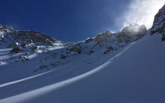 Snow-covered peaks and rocky outcrops under a clear blue sky, with mist rising from the slopes.