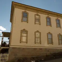 A large, yellow house with many windows and a stone foundation, under a clear blue sky.