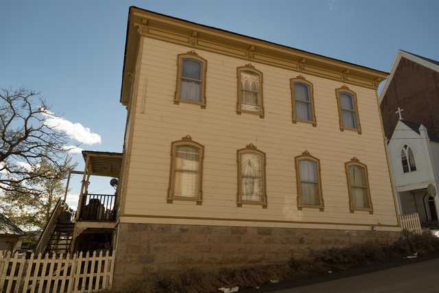 A large, yellow house with many windows and a stone foundation, under a clear blue sky.