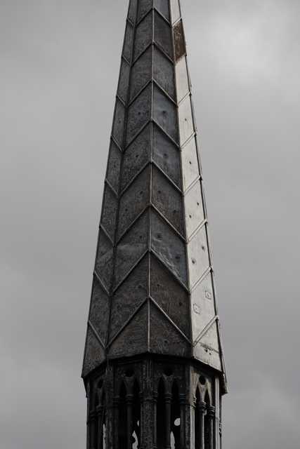 A tall, pointed spire constructed of weathered, diamond-patterned panels rises against a grey sky.