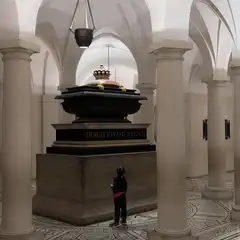 A child stands before the tomb of Horatio Viscount Nelson in a vaulted hall with columns and a patterned floor.