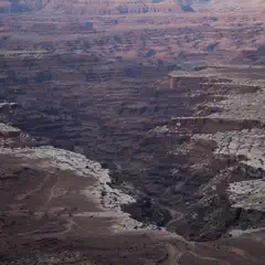 A canyon cuts through a plateau with reddish-brown rock formations and patches of white salt deposits.