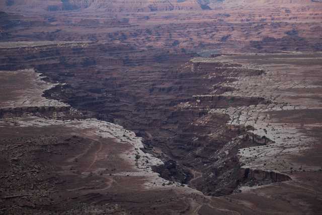 A canyon cuts through a plateau with reddish-brown rock formations and patches of white salt deposits.