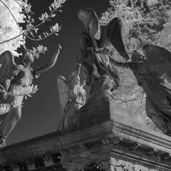 A stone monument features four winged figures in dynamic poses, partially framed by bare branches.