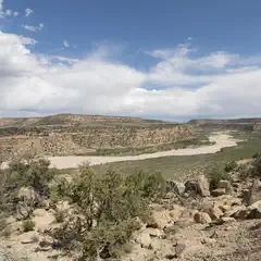 A dry riverbed winds through a desert landscape of rocky hills and sparse vegetation under a partly cloudy sky.