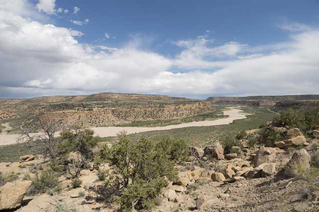 A dry riverbed winds through a desert landscape of rocky hills and sparse vegetation under a partly cloudy sky.
