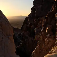 A narrow canyon frames a distant expanse of desert landscape under a yellow sky.