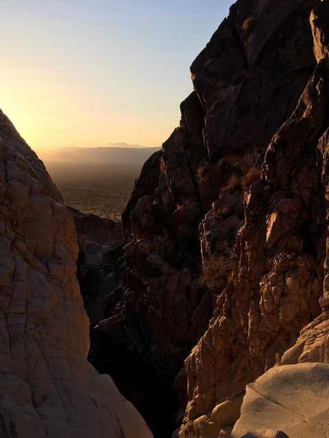 A narrow canyon frames a distant expanse of desert landscape under a yellow sky.