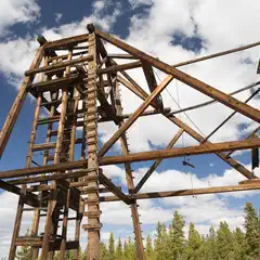 An old wooden mining headframe stands against a blue sky with white clouds.