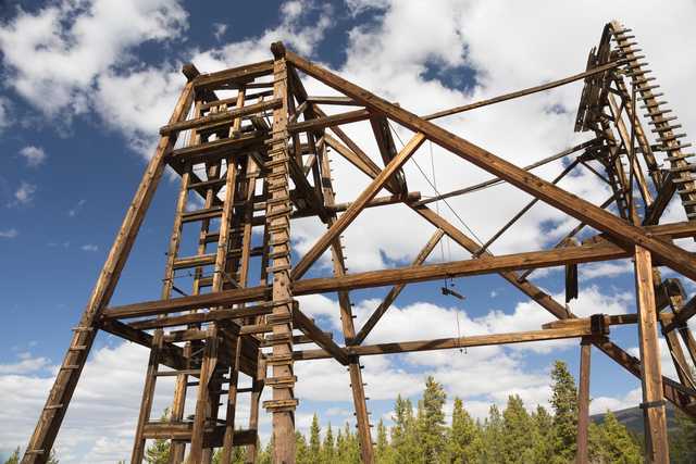 An old wooden mining headframe stands against a blue sky with white clouds.