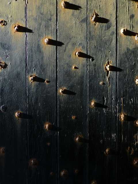 An old wooden door has several large metal studs protruding from it.