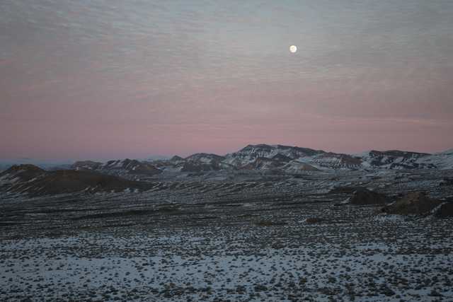 A snow-covered landscape with mountains in the distance under a pink and blue sky. The full moon is visible in the sky.