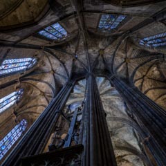 A grand cathedral interior with soaring stone columns, intricate ribbed vaults, and vibrant stained glass windows.