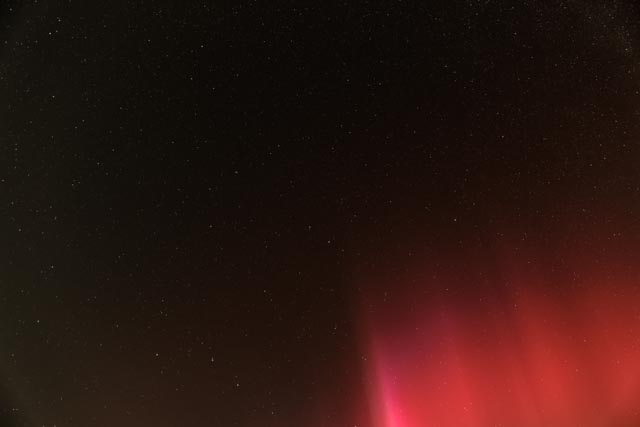 A night sky filled with stars and a vibrant red aurora.