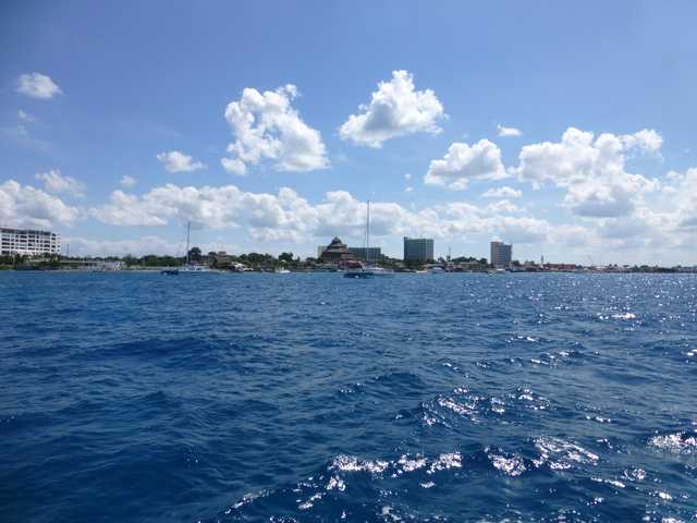 A calm sea under a cloudy sky, with boats and buildings on the horizon.