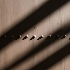 A wooden door with metal studs and bolts, partially shaded by sunlight filtering through slats above it.